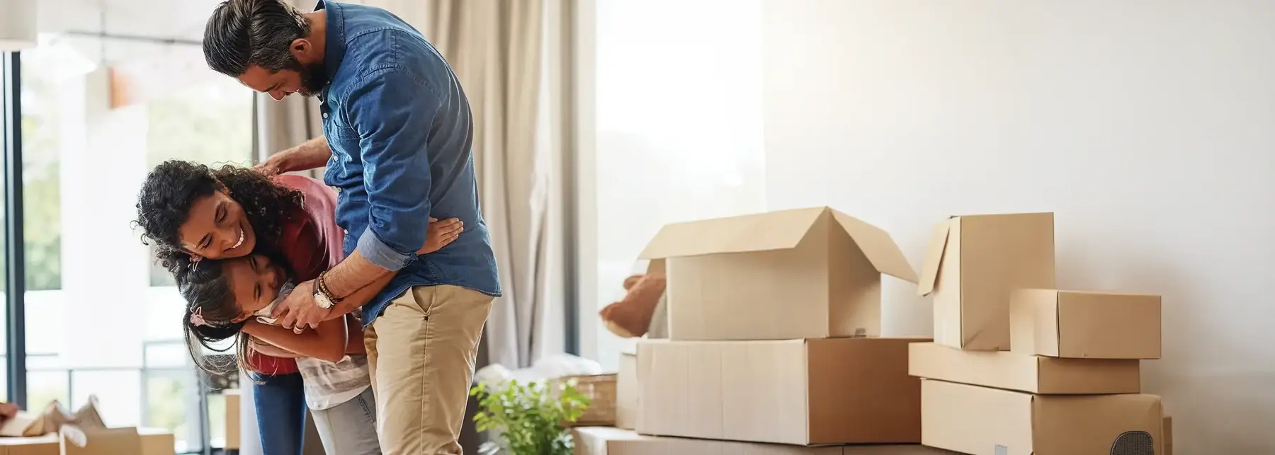 Family unpacking cardboard boxes during house move, with father and two children organizing belongings in bright living room with stacked boxes nearby