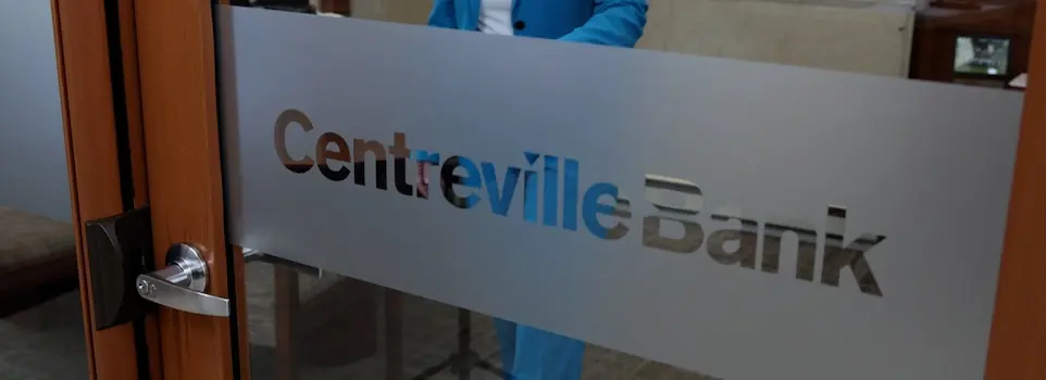 A woman in a blue suit opens a glass door etched with the Centreville Bank logo.