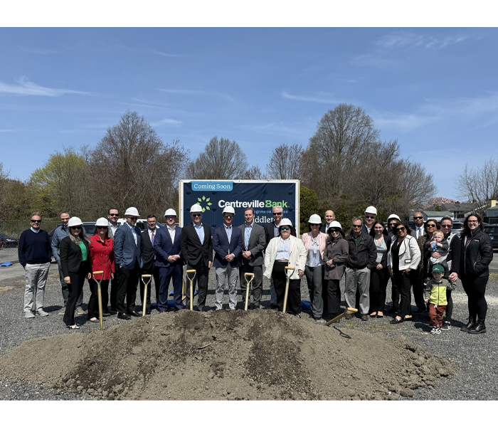 Group of people wearing hard hats posing behind a pile of dirt for a Centreville Bank groundbreaking ceremony.