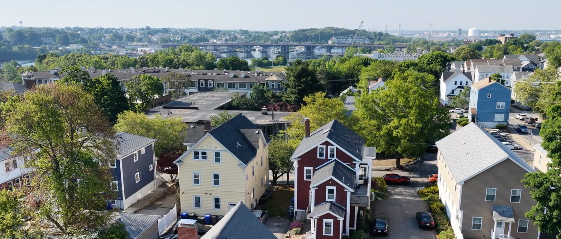Aerial view of a residential neighborhood with colorful houses, green trees, and streets in a suburban community under clear sky