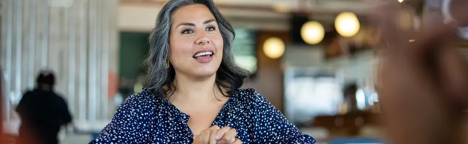 A woman talks with someone across a table in a modern open office.