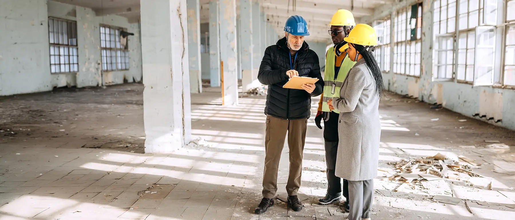 A contractor and a business owner review building plans inside a sunlit, empty commercial space under renovation.