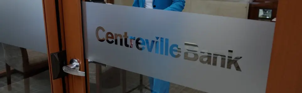A glass door etched with the Centreville Bank logo, held open into a branch lobby.