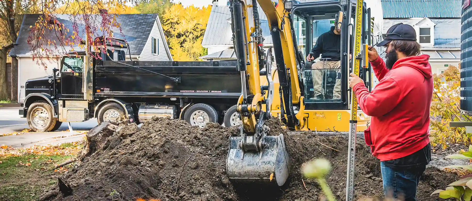 A construction worker at an excavation job site checks his phone next to an excavator and dump truck, illustrating managing commercial banking on the go.