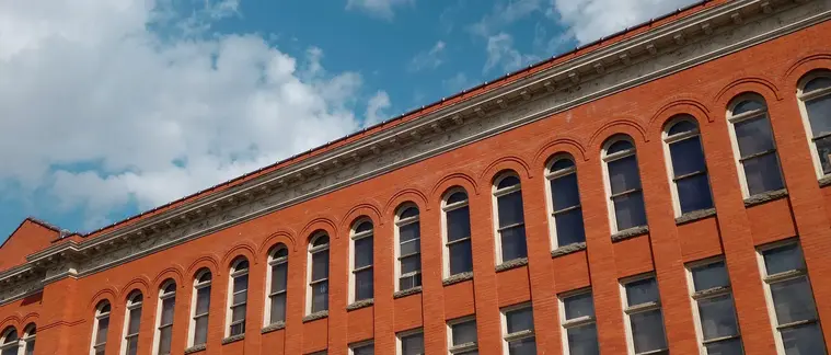 A low-angle view of a brick commercial building with rows of arched windows against a blue sky.