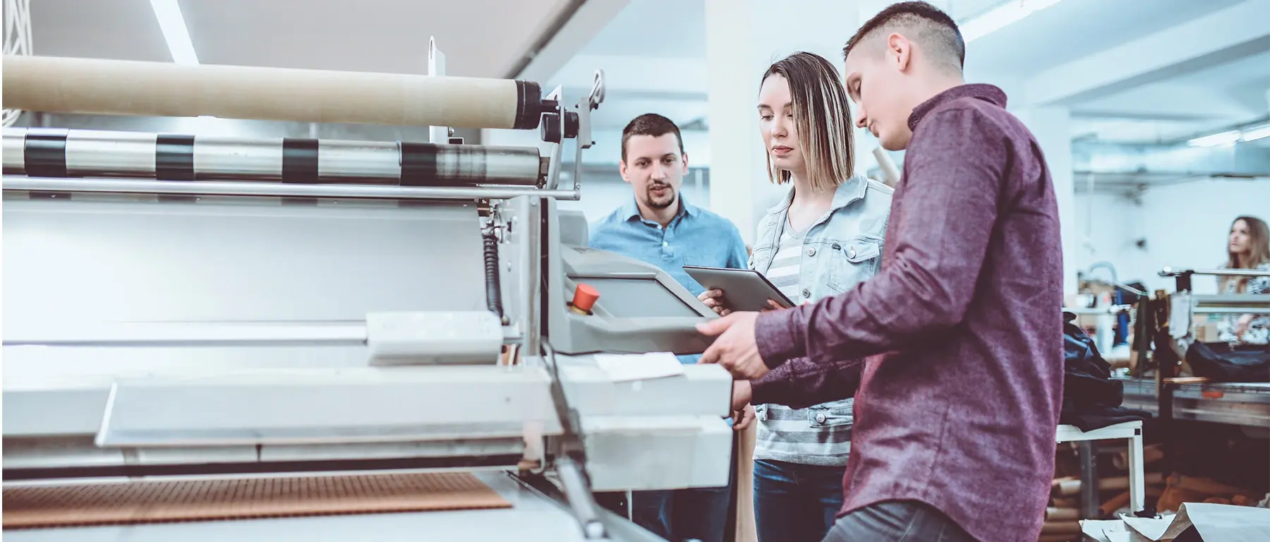 Three colleagues in a manufacturing workshop review fabric together at a large work table.