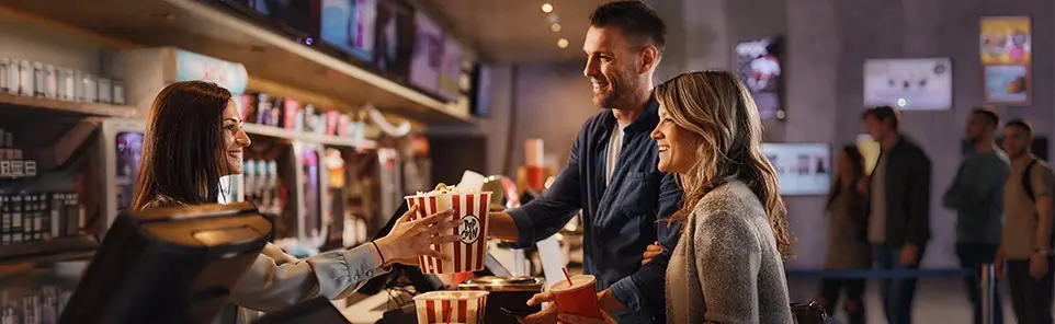 A couple buys popcorn from a staff member at a cinema concession counter.