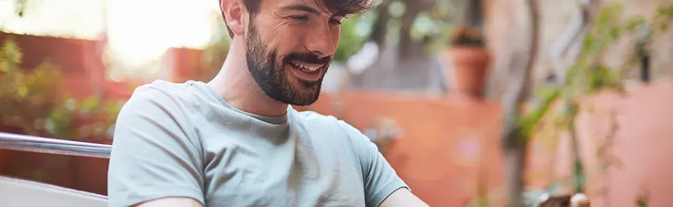 A smiling bearded man relaxes outdoors on a patio, reflecting the ease of managing account settings from anywhere.