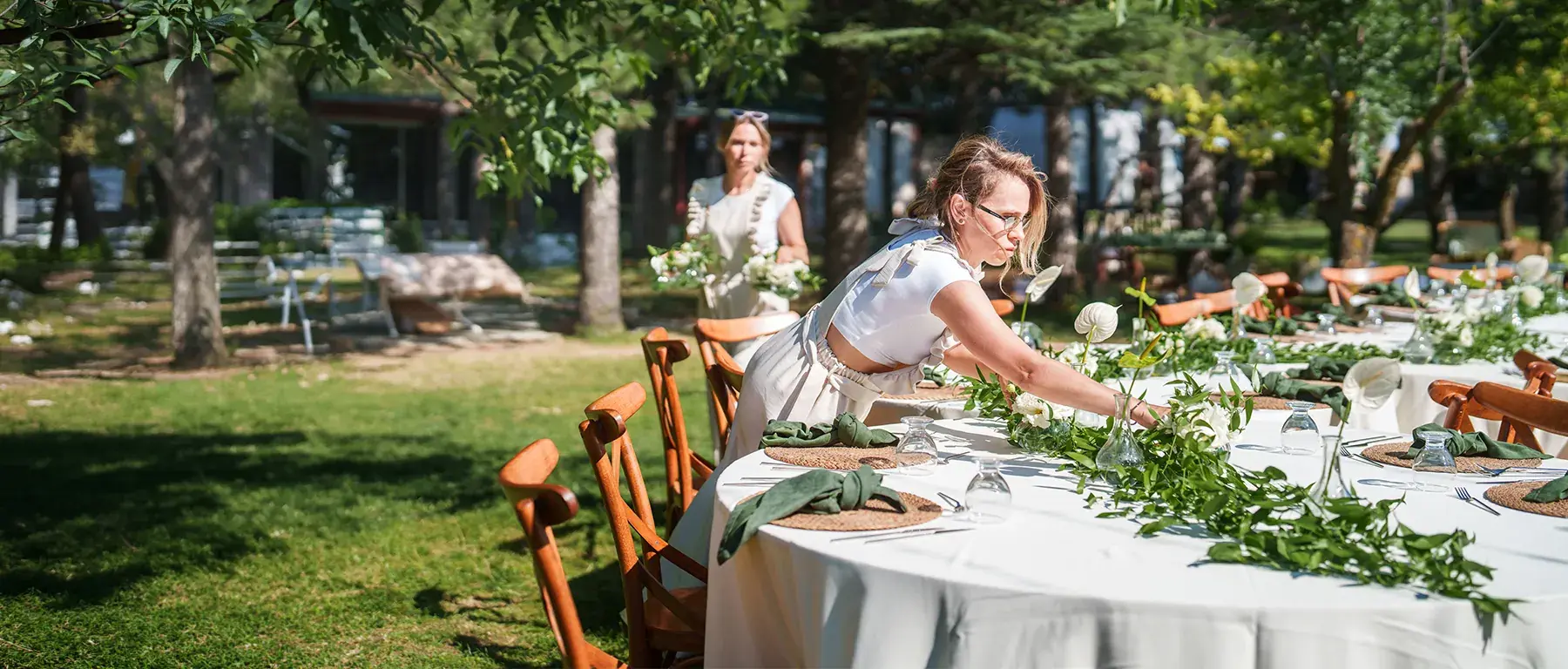 Two women arrange place settings and greenery at an outdoor event table, representing a small event-planning business using Zelle for Business payments.