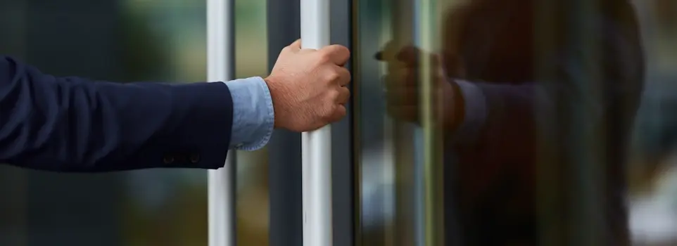 Man's hand pushing open a glass door or window, with a blurred reflection visible in the glass