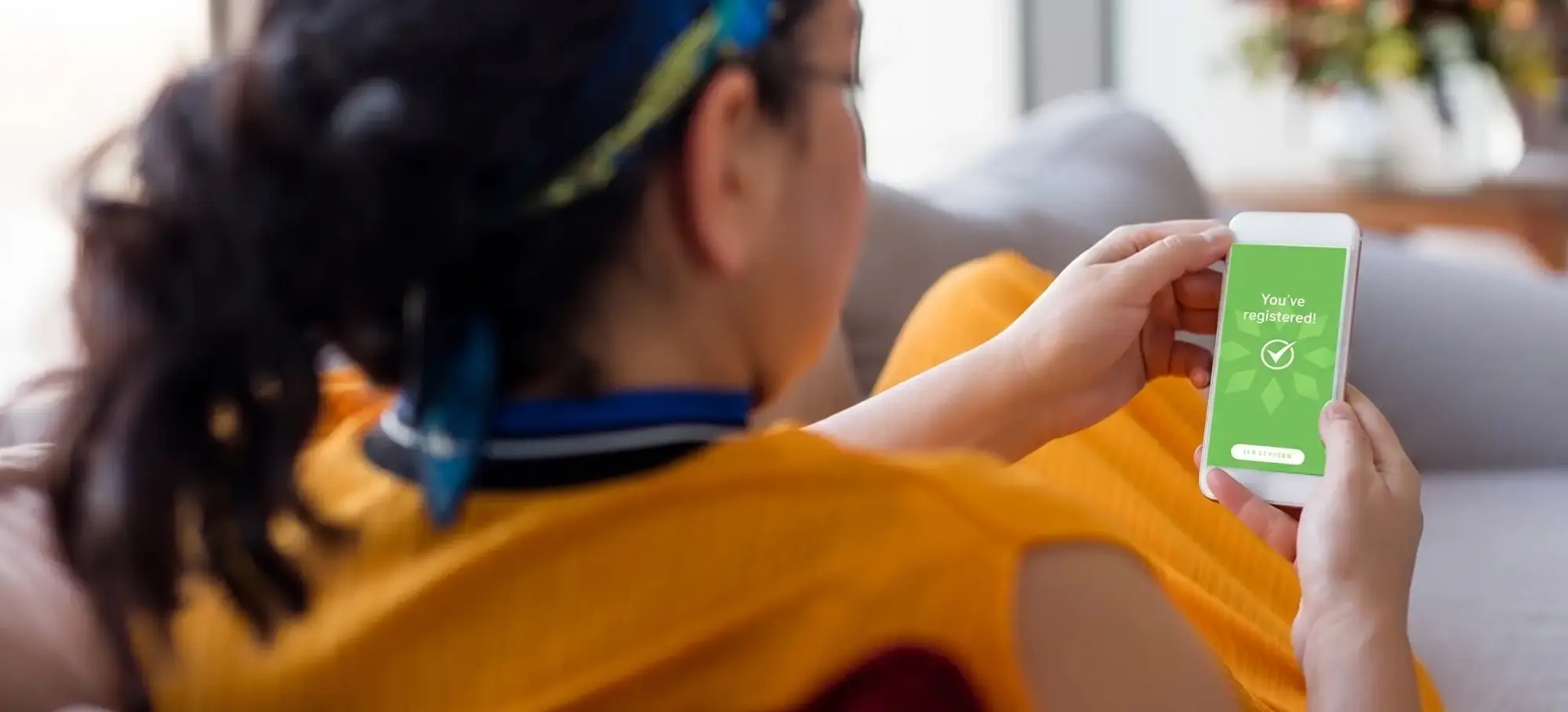 Person in yellow shirt holding green mobile phone displaying health or fitness app while sitting on couch