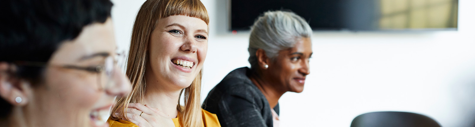 Three colleagues smile during a meeting in a bright conference room