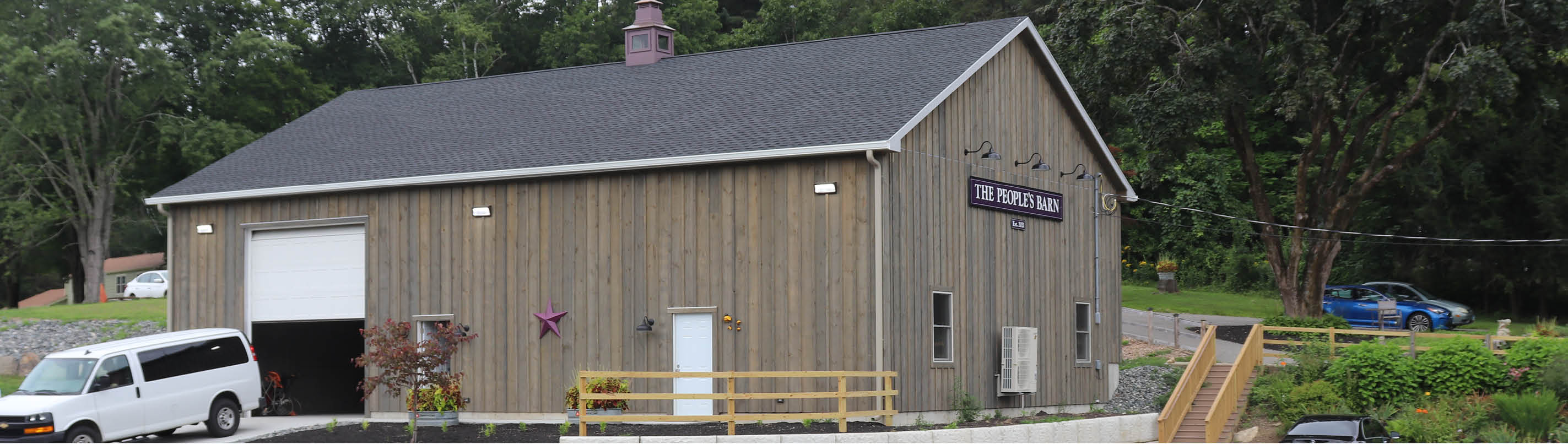 A timber barn building with a sign reading The People's Barn, a van parked by the open door