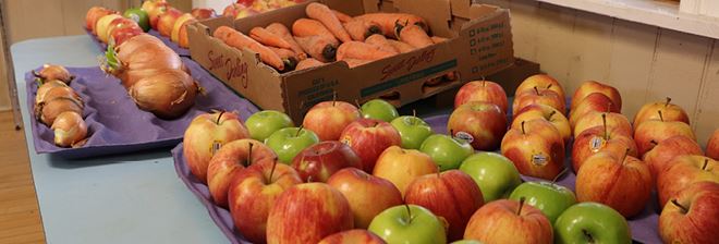 Apples, carrots and onions laid out in trays on tables at a food pantry