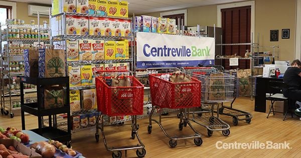Red carts and shelves of cereal in a food pantry, with a Centreville Bank banner on the wall behind them
