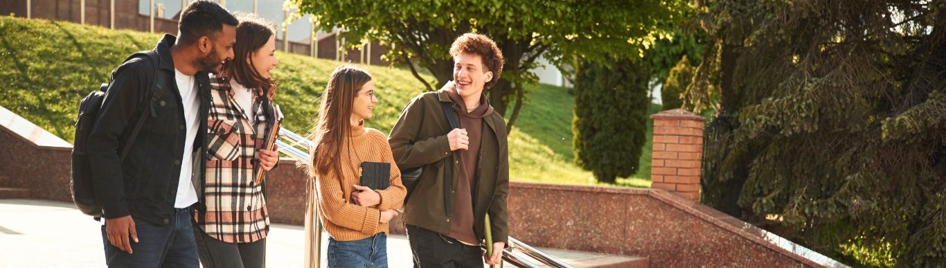Four students walk and talk together along a campus path on a sunny day